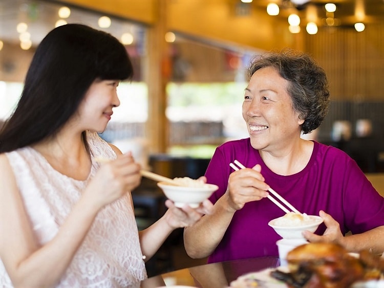 Young Chinese lady eating rice with older Chinese lady.